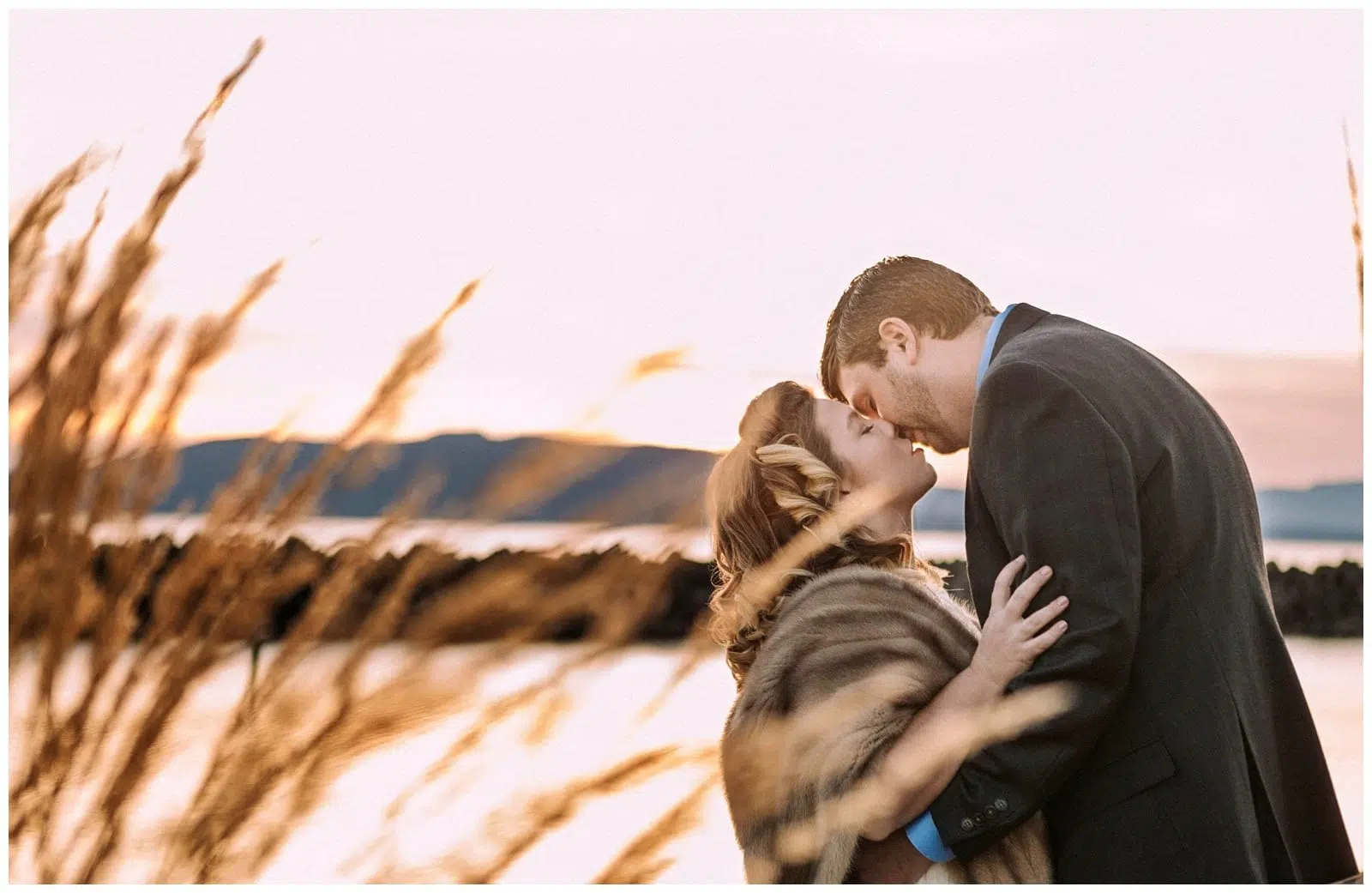 Premier Snohomish & Seattle Wedding Photographer | GSquared Weddings Photography A couple in formal attire shares a kiss at sunset by the water, with tall golden grass in the foreground and distant mountains behind—capturing a dreamy Snohomish Seattle wedding engagement moment. 47.9129° N, 122.0982° W | Serving Snohomish, Seattle , Orlando & Beyond
