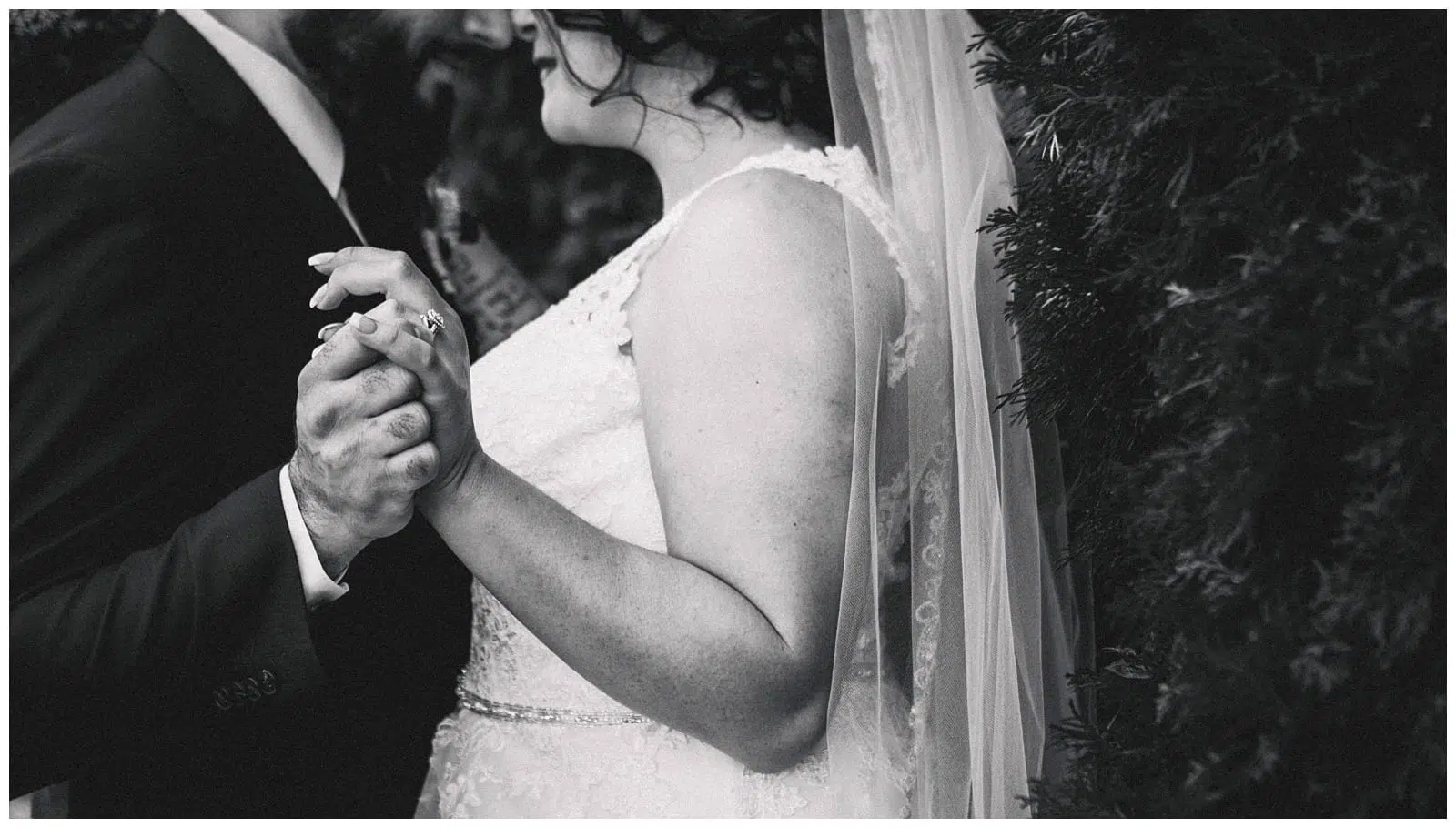 Premier Snohomish & Seattle Wedding Photographer | GSquared Weddings Photography Black-and-white photo of a bride and groom holding hands while dancing at their Snohomish wedding, with the bride in a lace dress and veil, and the groom wearing a suit. Their faces are partially visible and close together. 47.9129° N, 122.0982° W | Serving Snohomish, Seattle , Orlando & Beyond