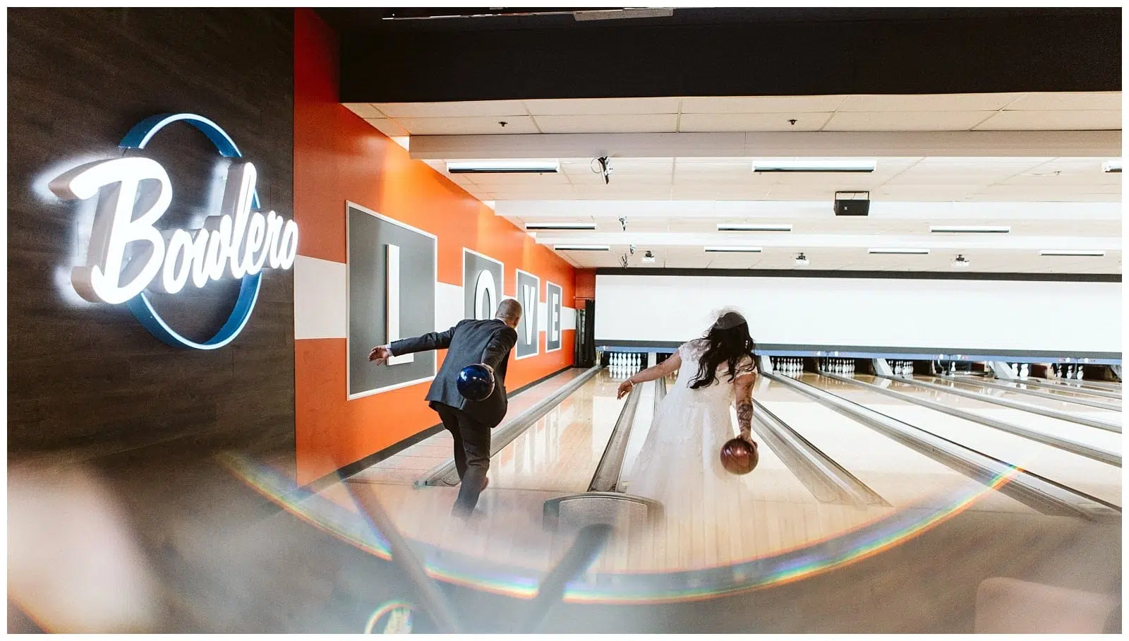 Premier Snohomish & Seattle Wedding Photographer | GSquared Weddings Photography A bride and groom in wedding attire bowl side by side at a modern bowling alley near Snohomish Seattle. The groom sports a suit, the bride a white dress and veil, with Bowlero lit up on the wall—a fun twist on their wedding engagement. 47.9129° N, 122.0982° W | Serving Snohomish, Seattle , Orlando & Beyond