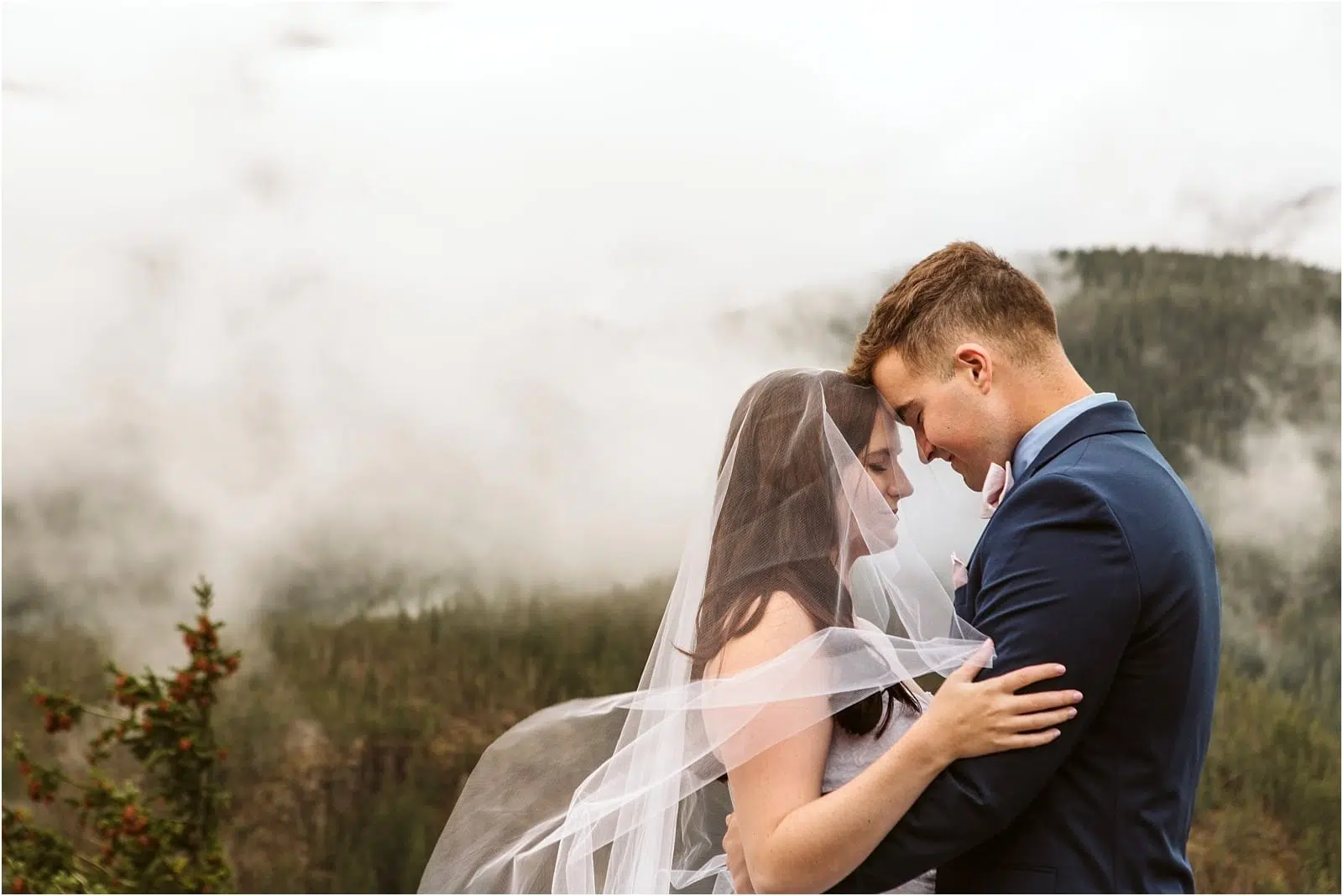 Premier Snohomish & Seattle Wedding Photographer | GSquared Weddings Photography A bride and groom embrace outdoors in this dreamy Snohomish Seattle wedding scene. Her veil blows in the wind, with misty mountains and dense trees creating a breathtaking backdrop. 47.9129° N, 122.0982° W | Serving Snohomish, Seattle , Orlando & Beyond