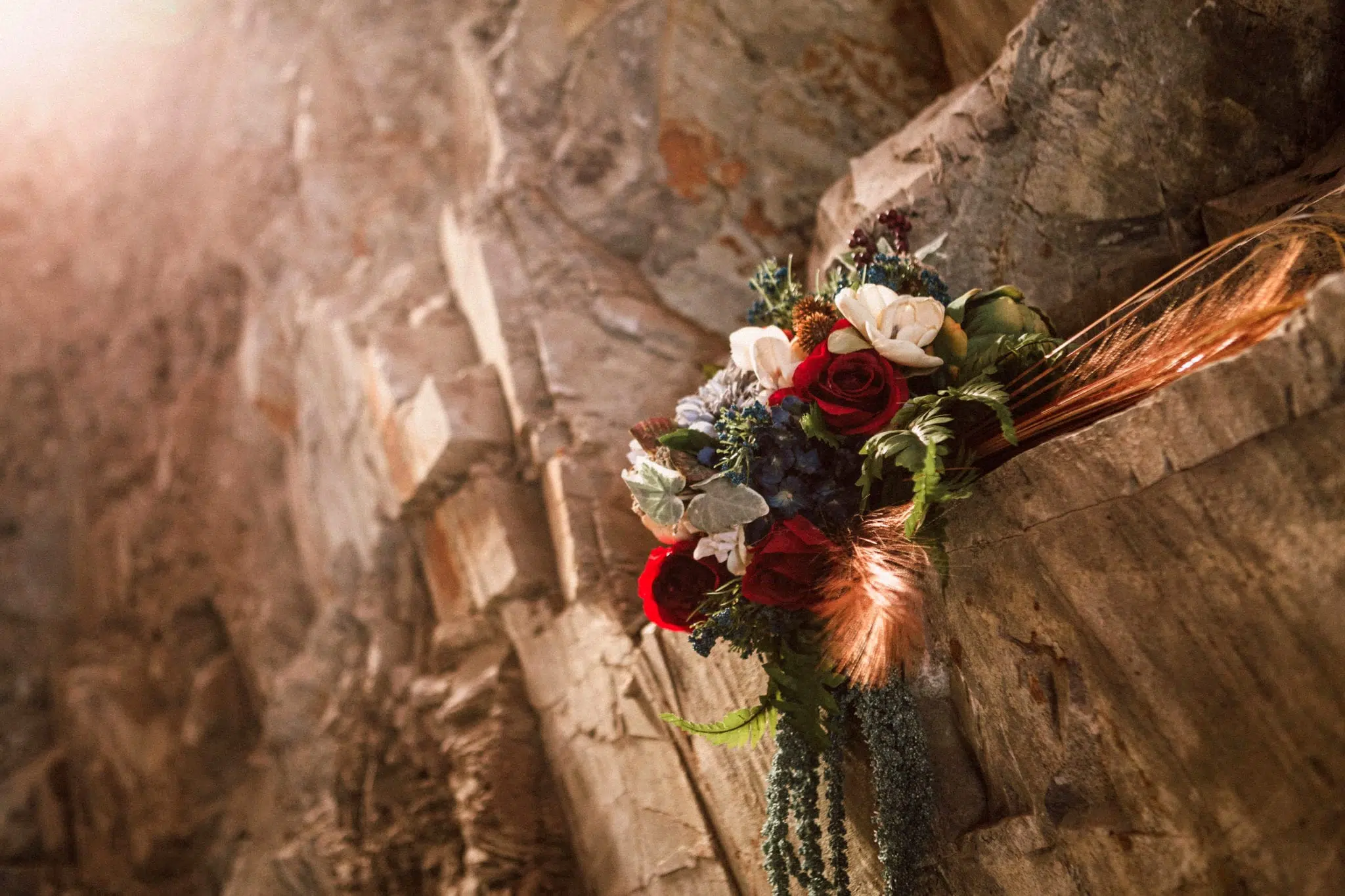 Premier Snohomish & Seattle Wedding Photographer | GSquared Weddings Photography A bouquet of red, white, and purple flowers with greenery rests on a rocky ledge, illuminated by warm sunlight—perfect for a Snohomish or Seattle wedding engagement. 47.9129° N, 122.0982° W | Serving Snohomish, Seattle , Orlando & Beyond