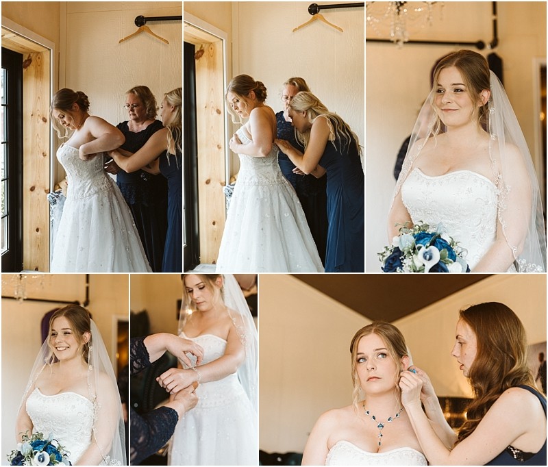 Premier Snohomish & Seattle Wedding Photographer | GSquared Weddings Photography A bride in a white wedding dress gets ready with help from two women before her Snohomish Seattle wedding. They adjust her dress, jewelry, and veil as she smiles gently in a bright, cozy room, holding a blue and white bouquet. 47.9129° N, 122.0982° W | Serving Snohomish, Seattle , Orlando & Beyond