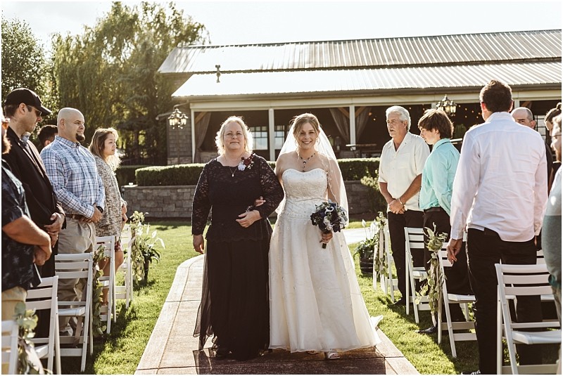 Premier Snohomish & Seattle Wedding Photographer | GSquared Weddings Photography A smiling bride in a white dress walks down an outdoor aisle with an older woman at a Snohomish wedding, while guests stand and watch on both sides under sunlight. 47.9129° N, 122.0982° W | Serving Snohomish, Seattle , Orlando & Beyond