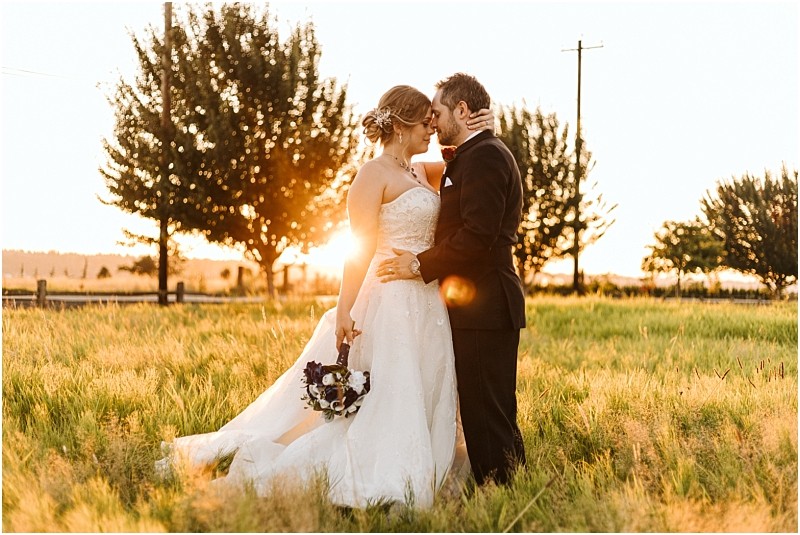 Premier Snohomish & Seattle Wedding Photographer | GSquared Weddings Photography Bride and groom embrace in a grassy field at sunset during their Snohomish wedding. The bride holds a bouquet and wears a white strapless gown, while the groom is in a dark suit. Trees and golden sunlight create a warm, romantic atmosphere. 47.9129° N, 122.0982° W | Serving Snohomish, Seattle , Orlando & Beyond