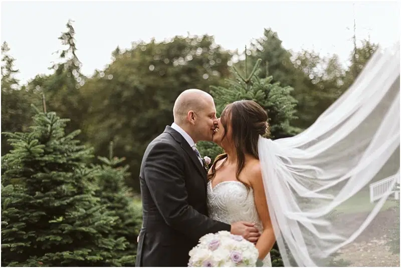 Premier Snohomish & Seattle Wedding Photographer | GSquared Weddings Photography A bride and groom kiss outdoors among evergreen trees at their romantic Snohomish wedding. The bride’s strapless gown and flowing veil, paired with the groom’s dark suit, create a timeless Seattle engagement moment surrounded by nature. 47.9129° N, 122.0982° W | Serving Snohomish, Seattle , Orlando & Beyond