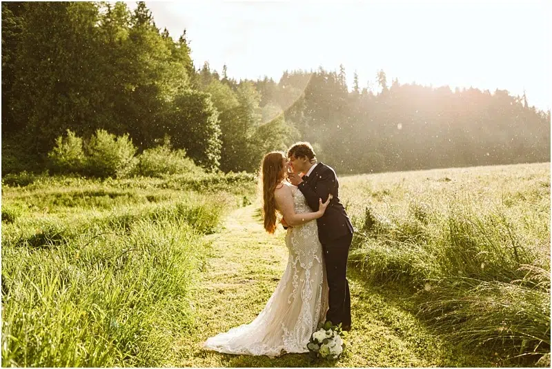 Snohomish & Seattle Wedding Photographer | GSquared Weddings Photography A bride and groom embrace on a sunlit grassy path at Marionfield Farm, surrounded by lush greenery, with a wedding bouquet at their feet and warm sunlight streaming through the trees—a perfect elopement moment. 47.9129° N, 122.0982° W | wedding photo by GSquared Weddings