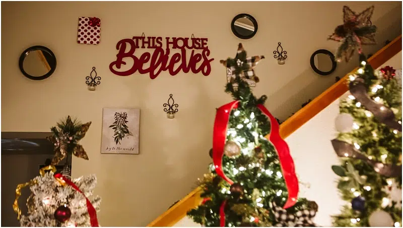 A cozy indoor scene in Snohomish with decorated Christmas trees, red and white ribbons, and a wall sign that reads This House Believes. Small mirrors and wall ornaments adorn the background. Snohomish Wedding Photography