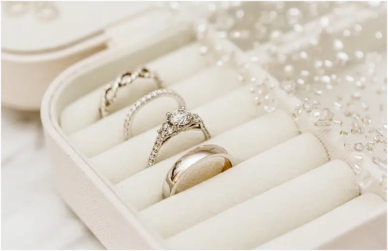 Three elegant rings, including a diamond engagement ring, a diamond-studded wedding band, and a plain wedding band, displayed in a cream-colored velvet jewelry box with delicate beaded fabric nearby in charming Snohomish. Snohomish Wedding Photography