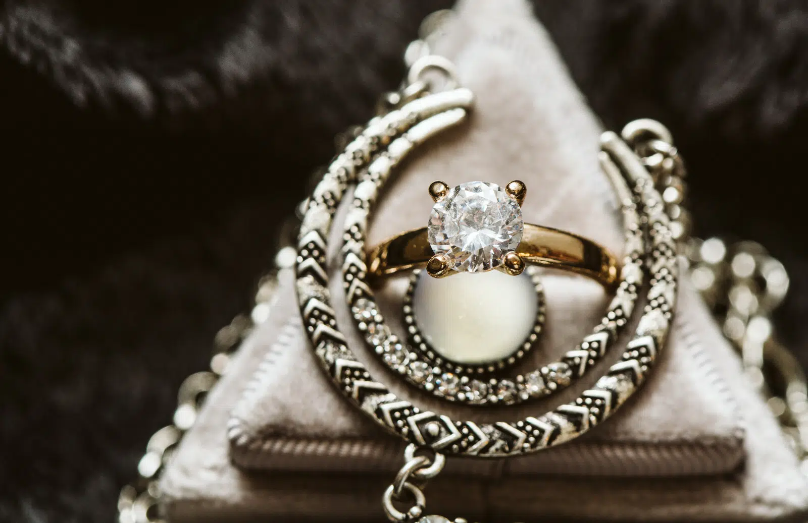 A gold ring with a large, round diamond is displayed on a soft, triangular jewelry stand in Snohomish, surrounded by intricately patterned silver bangles and chains. Snohomish Wedding Photography