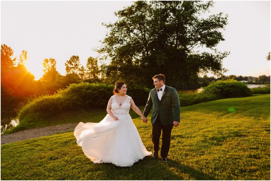 Glam Wedding at Pemberton Farm bride and groom walking in the sunset on the grass with a tree and river behind them illuminated by warm glowing evening light