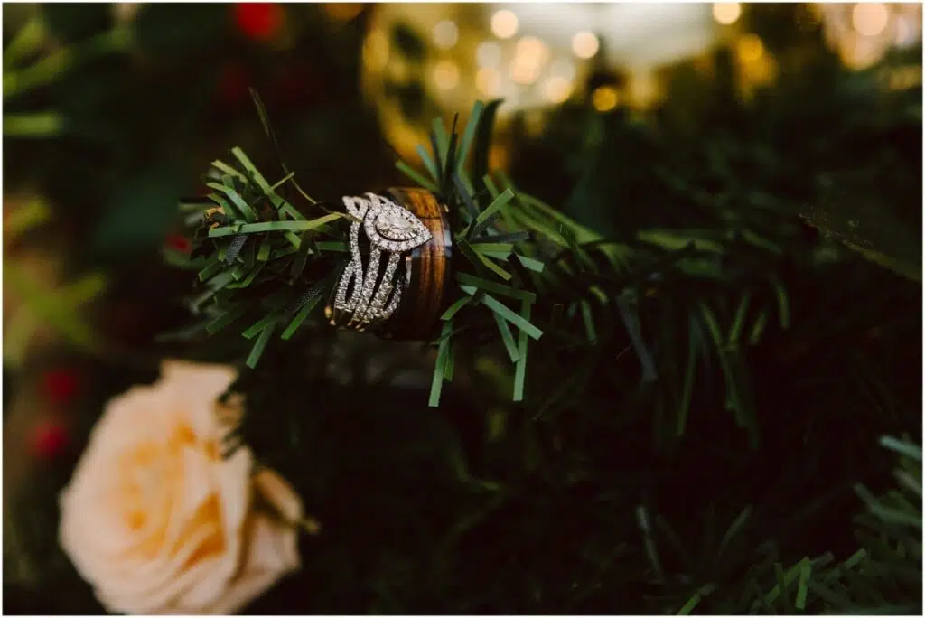 winter wedding with pear shaped diamond bridal wedding ring and wood inset men's wedding band on a Christmas tree branch with Christmas lights twinkling in the background