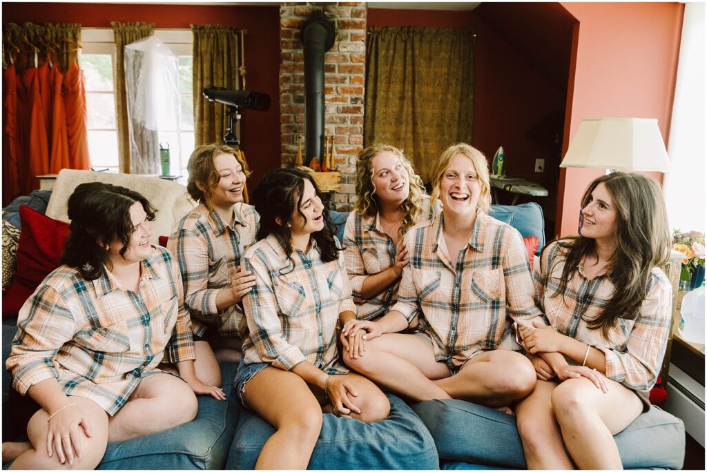 Snohomish Wedding Photographer GSquared Weddings Six people are sitting on a couch, wearing matching plaid shirts and shorts, casually chatting and laughing together. The room has a cozy, rustic vibe with a brick column and warm-toned walls. Serving Seattle, Snohomish and Orlando