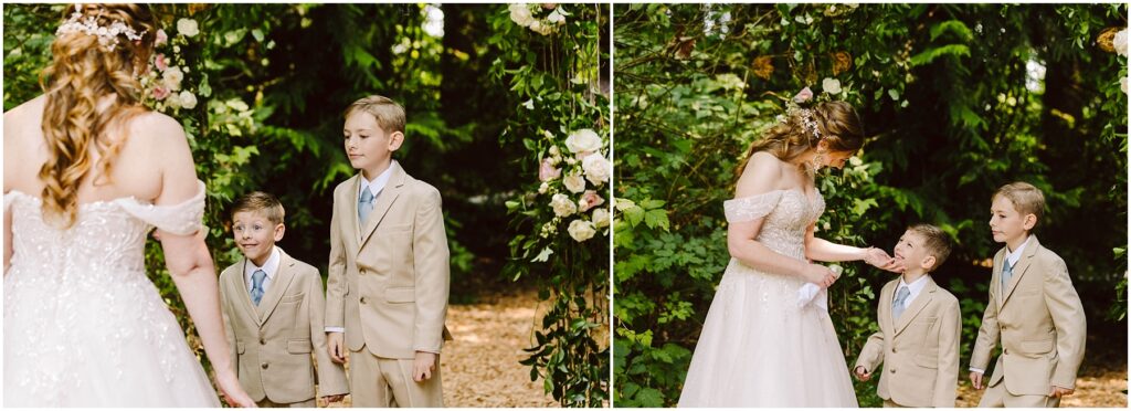 Snohomish Wedding Photographer GSquared Weddings A bride in an off-shoulder gown stands with two young boys in beige suits in a lush, green outdoor setting. They are under an arch adorned with flowers, as the bride interacts with the boys who look up at her. Serving Seattle, Snohomish and Orlando