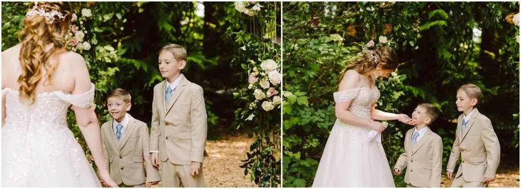 Snohomish Wedding Photographer GSquared Weddings A bride in an off-shoulder gown stands with two young boys in beige suits in a lush, green outdoor setting. They are under an arch adorned with flowers, as the bride interacts with the boys who look up at her. Serving Seattle, Snohomish and Orlando