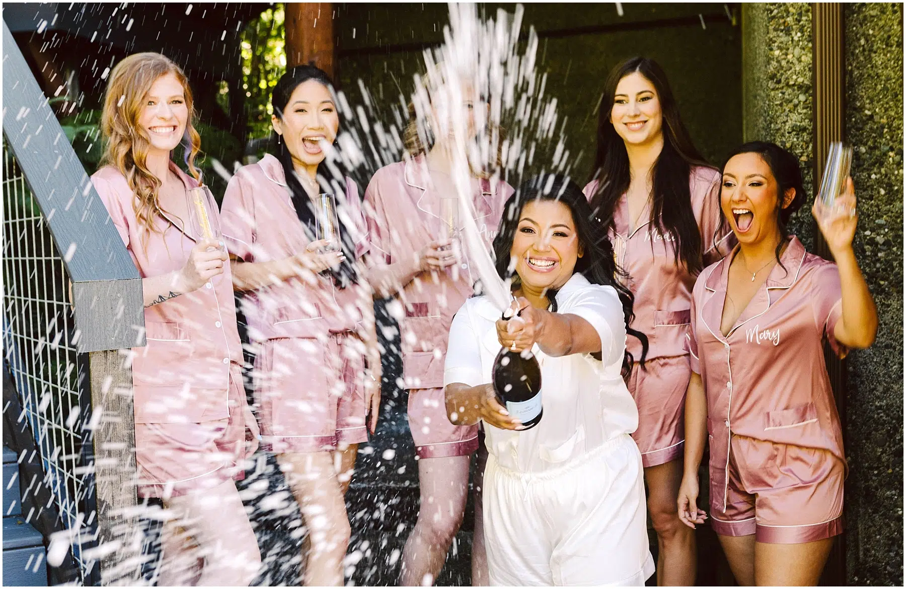 Snohomish Wedding Photographer GSquared Weddings A woman in white pajamas joyfully pops open a champagne bottle spraying it around her Five women in matching pink pajamas laugh and react with excitement They are outside with greenery and a wooden structure in the background Serving Seattle Snohomish and Orlando Snohomish Wedding Photographer GSquared Weddings A woman in white pajamas joyfully pops open a champagne bottle spraying it around her Five women in matching pink pajamas laugh and react with excitement They are outside with greenery and a wooden structure in the background Serving Seattle Snohomish and Orlando