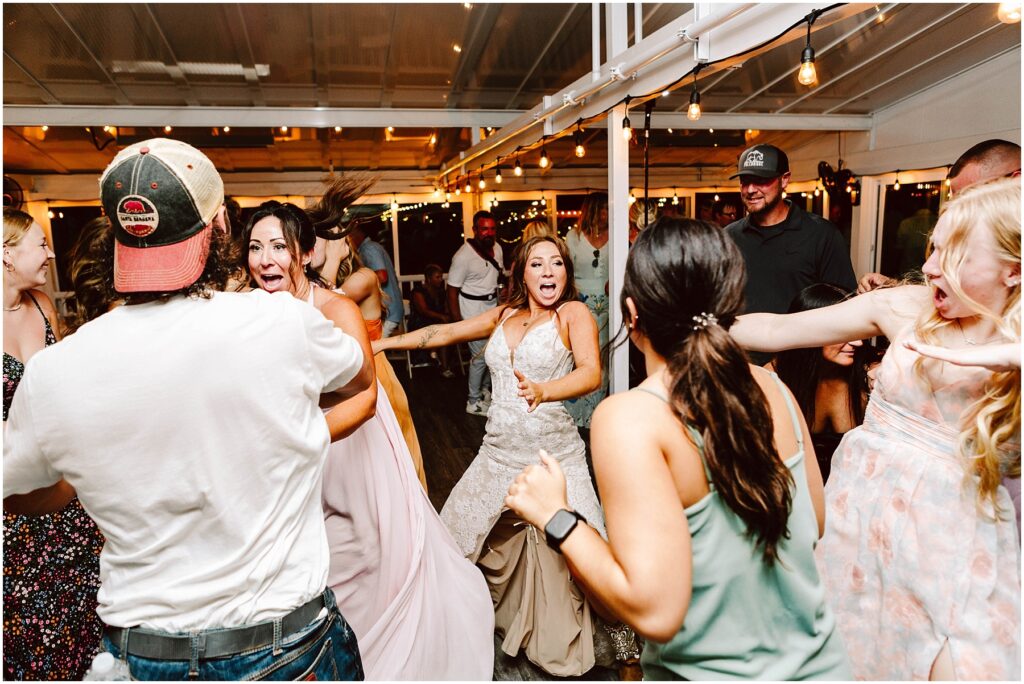 Snohomish Wedding Photographer GSquared Weddings A lively wedding reception with a bride in a white dress energetically dancing among guests. People around her are laughing and moving joyfully. String lights illuminate the festive atmosphere. Serving Seattle, Snohomish and Orlando