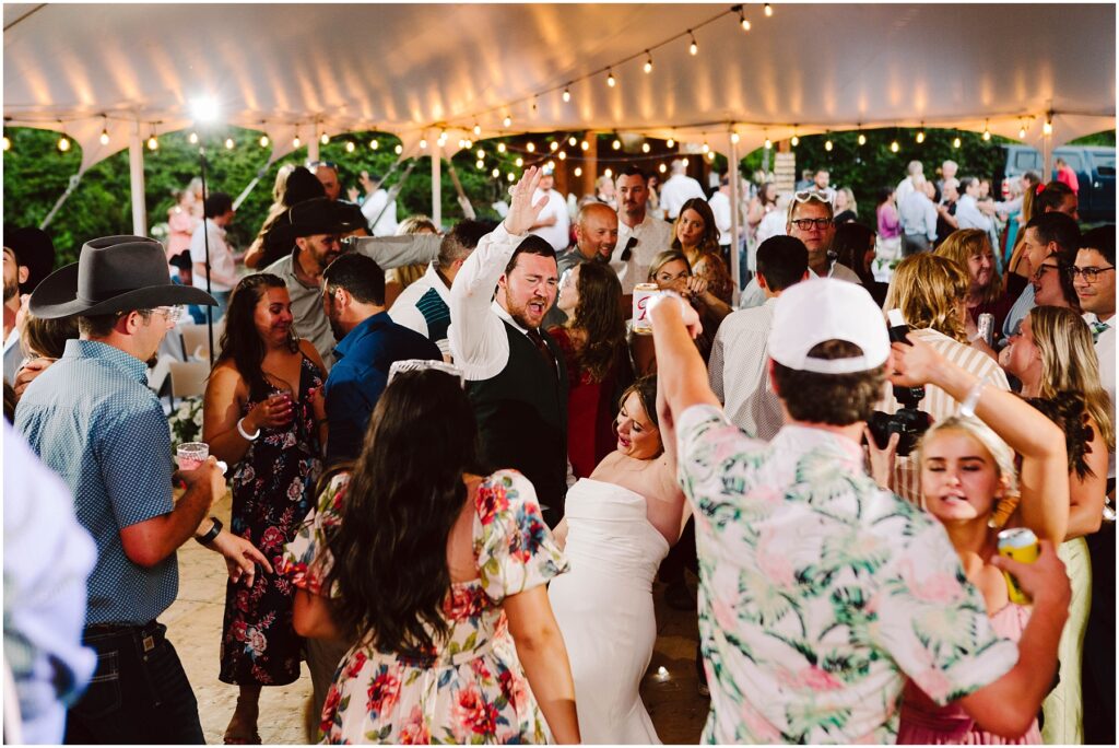 Snohomish Wedding Photographer GSquared Weddings A lively wedding reception under a tent with string lights. Guests are dancing energetically, with one person lifting their arm in celebration. The crowd includes people in festive attire, capturing the joyful atmosphere. Serving Seattle, Snohomish and Orlando