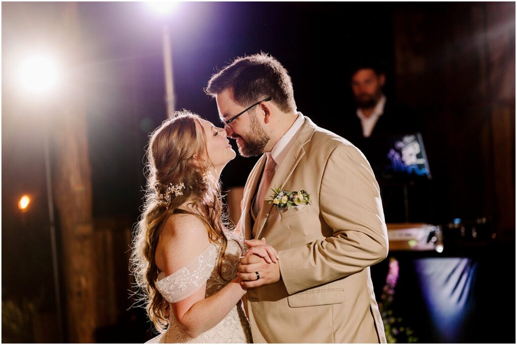 Snohomish Wedding Photographer GSquared Weddings A couple shares a romantic dance at a wedding. The woman, in a white gown with floral details, and the man, in a beige suit with a boutonnière, gently lean in close to each other. Soft lighting highlights their expressions. Serving Seattle, Snohomish and Orlando