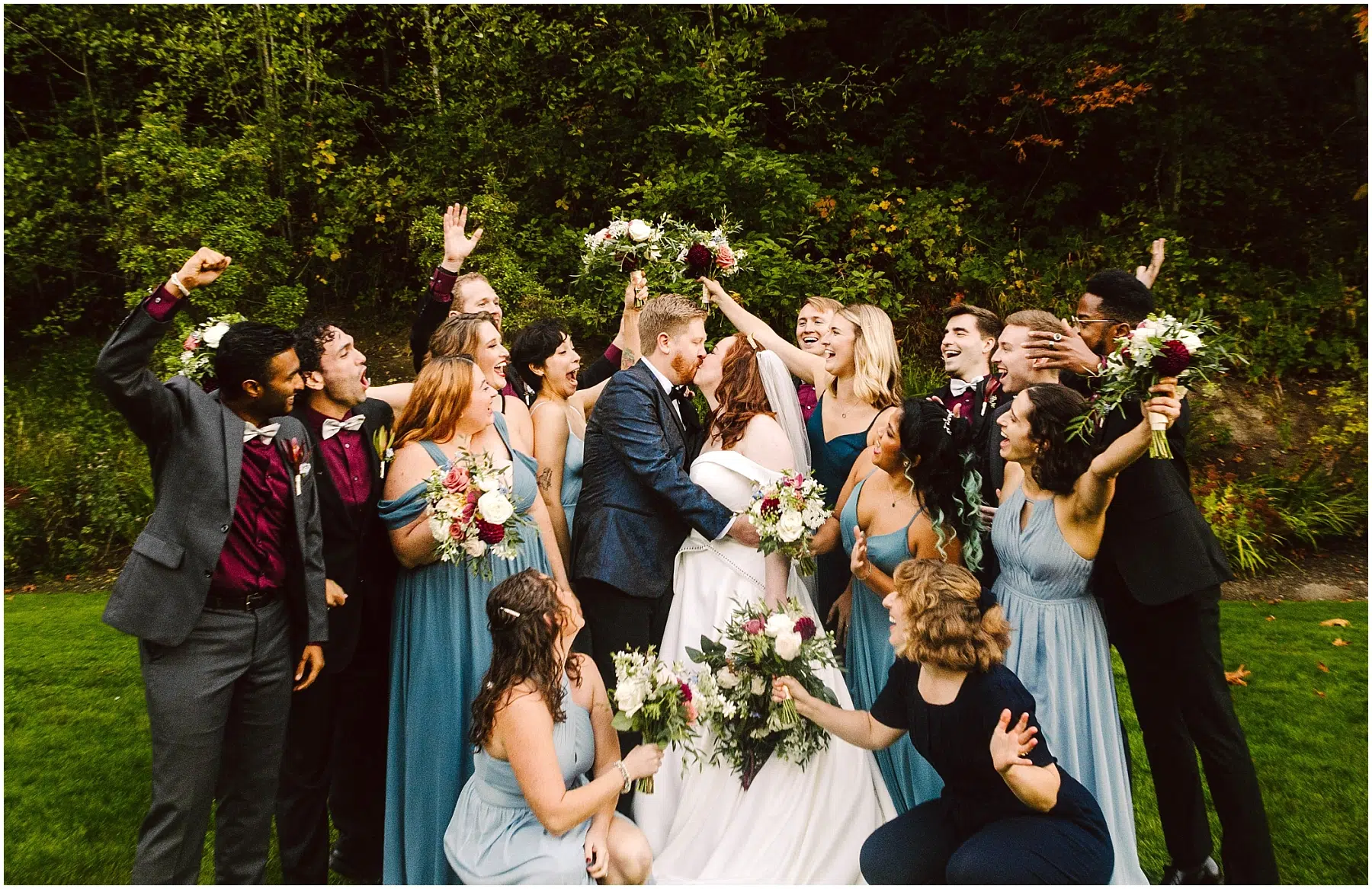 Snohomish Wedding Photographer GSquared Weddings A wedding party poses outdoors with the bride and groom kissing in the center Bridesmaids in blue dresses and groomsmen in dark suits cheer and hold bouquets against a green leafy background Everyone appears joyful and celebratory Serving Seattle Snohomish and Orlando Snohomish Wedding Photographer GSquared Weddings A wedding party poses outdoors with the bride and groom kissing in the center Bridesmaids in blue dresses and groomsmen in dark suits cheer and hold bouquets against a green leafy background Everyone appears joyful and celebratory Serving Seattle Snohomish and Orlando