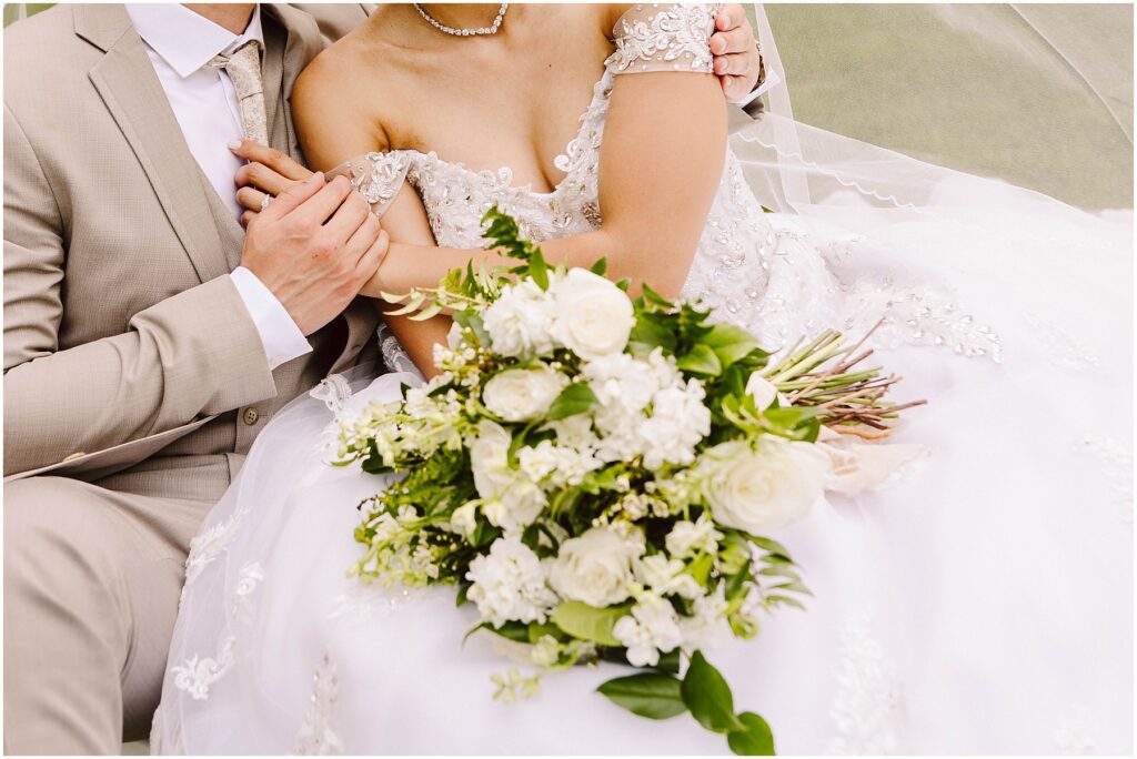 Snohomish Wedding Photographer GSquared Weddings A bride in a detailed white gown and a groom in a beige suit sit closely. The bride holds a bouquet of white and green flowers. Their heads arent visible in the frame. Serving Seattle, Snohomish and Orlando
