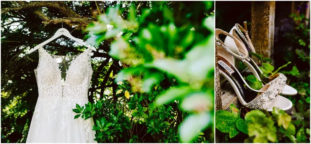 Snohomish Wedding Photographer GSquared Weddings A bridal gown with intricate lace details hangs from a tree branch, surrounded by lush green foliage. Beside it, sparkling high-heeled shoes rest on a wooden surface, partially covered by greenery. Serving Seattle, Snohomish and Orlando