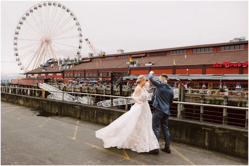 Snohomish Wedding Photographer GSquared Weddings A couple dances outside near a waterfront. The woman wears a white wedding dress, and the man is in a blue suit. In the background, theres a large Ferris wheel and a building with a sign that reads The Crab Pot. Serving Seattle, Snohomish and Orlando