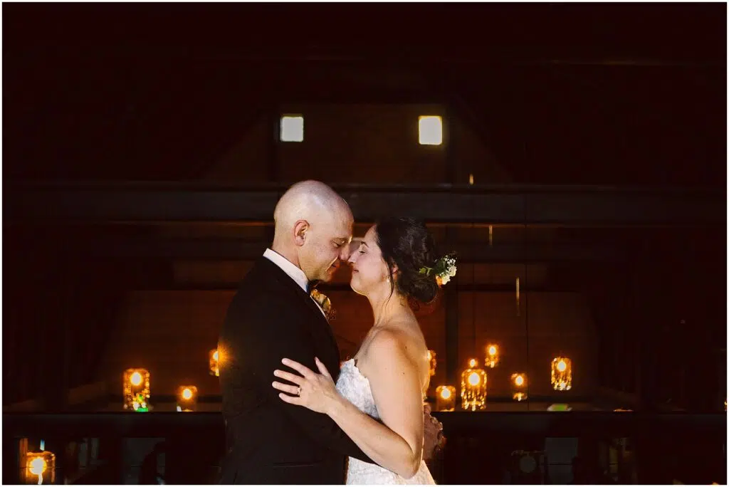 Snohomish Wedding Photographer GSquared Weddings A couple in formal attire shares a tender moment, gently touching foreheads. The dimly lit background features a row of glowing lights and candles, creating a romantic atmosphere. Serving Seattle, Snohomish and Orlando