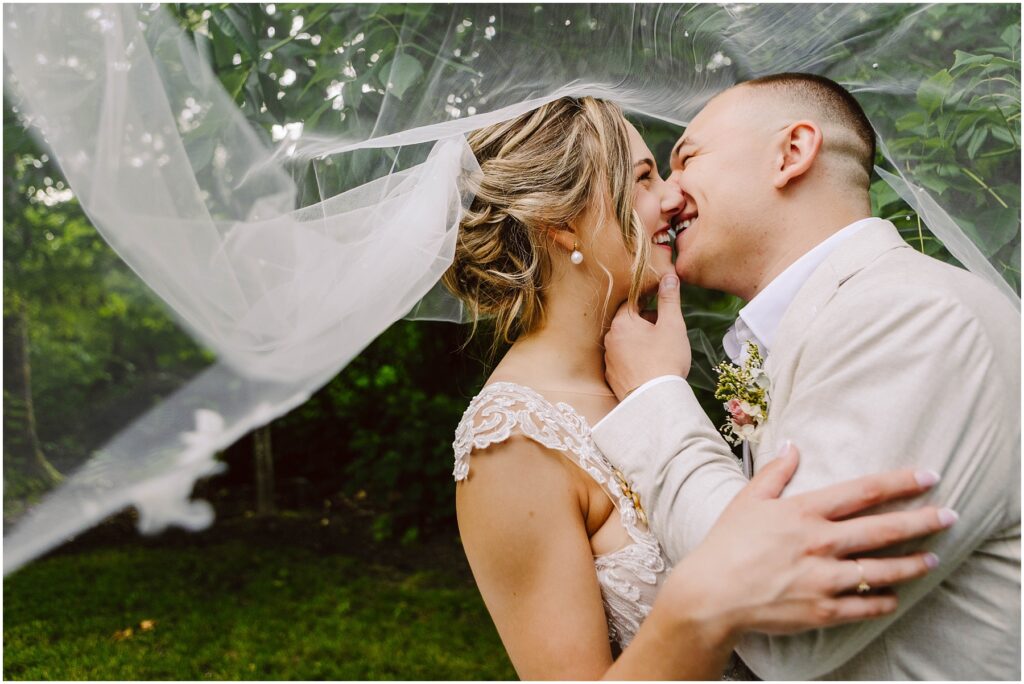 Snohomish Wedding Photographer GSquared Weddings A bride and groom share a joyful moment under a veil. The bride is gently touching the grooms face, and both are smiling, standing closely together. The background is lush with greenery. Serving Seattle, Snohomish and Orlando