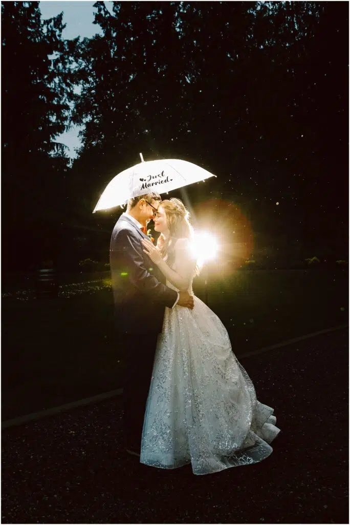 Snohomish Wedding Photographer GSquared Weddings A bride and groom embrace under a glowing umbrella that reads Just Married, with a soft light shining behind them. They are standing on a dark path surrounded by trees. The bride is wearing a white gown, and the groom is in a suit. Serving Seattle, Snohomish and Orlando