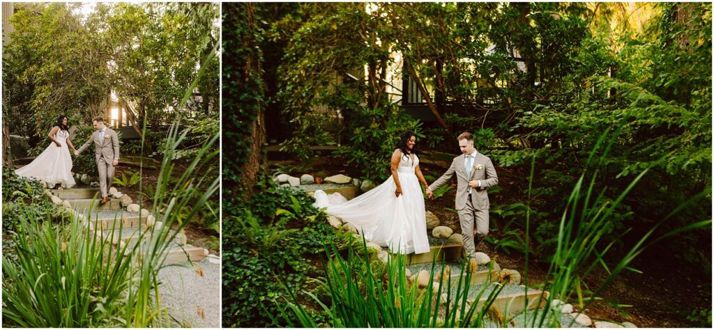Snohomish Wedding Photographer GSquared Weddings A couple walks down a garden path. The woman wears a long, flowing white dress, and the man wears a light brown suit. They hold hands, surrounded by lush green foliage and soft evening light filtering through the trees. Serving Seattle, Snohomish and Orlando