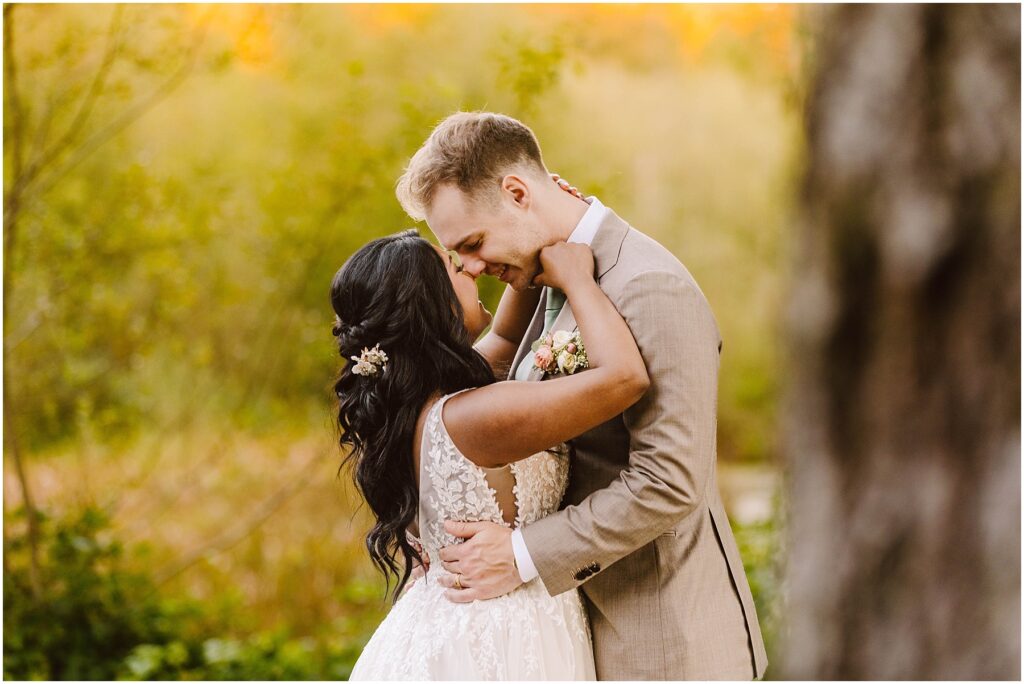 Snohomish Wedding Photographer GSquared Weddings A bride and groom embrace tenderly outdoors. The bride wears a white lace gown with a floral hairpiece, and the groom is in a light tan suit. They are surrounded by soft, blurred greenery, creating a romantic and intimate atmosphere. Serving Seattle, Snohomish and Orlando