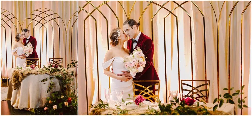Snohomish Wedding Photographer GSquared Weddings A bride and groom embrace in front of a decorated table with floral arrangements. The groom wears a red velvet suit, and the bride holds a bouquet. They stand beneath a gold arch, dressed in elegant wedding attire. Serving Seattle, Snohomish and Orlando