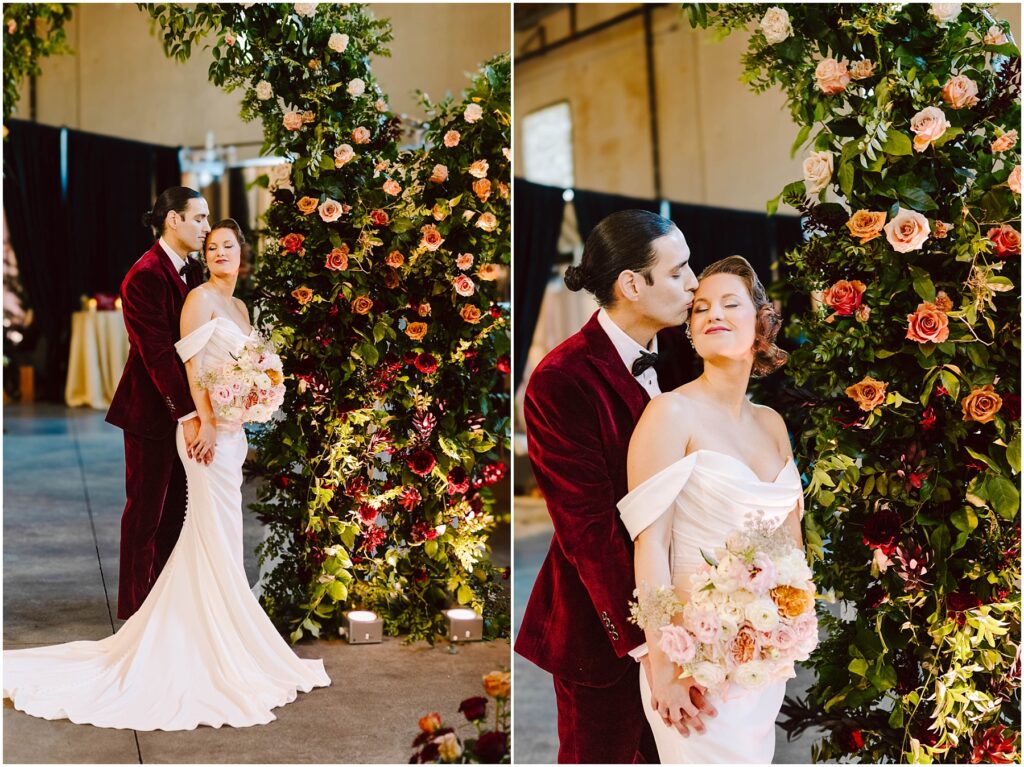 Snohomish Wedding Photographer GSquared Weddings A couple stands together in an elegant setting. The person in a white gown holds a bouquet of flowers, while the person in a burgundy suit embraces them. They are surrounded by a floral arch with various blossoms. Serving Seattle, Snohomish and Orlando