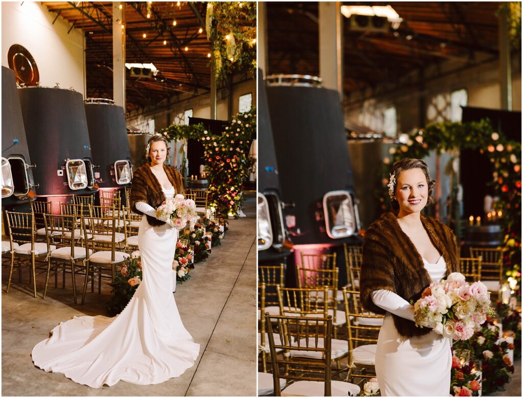 Snohomish Wedding Photographer GSquared Weddings A bride stands in an elegant industrial venue wearing a white gown and fur shawl, holding a bouquet of pink and white flowers. The aisle is lined with gold chairs and floral arrangements. The ceiling is adorned with greenery. Serving Seattle, Snohomish and Orlando