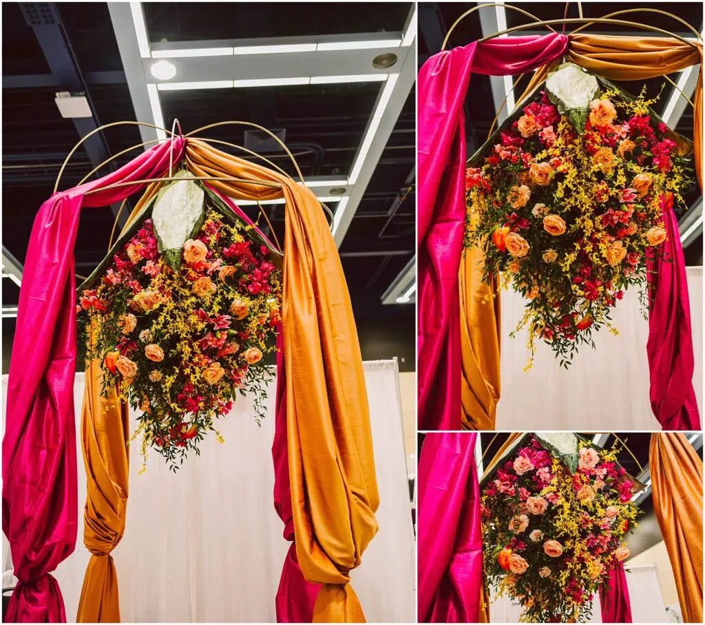 Snohomish Wedding Photographer GSquared Weddings A decorative archway draped with vibrant pink and orange fabric features a lush arrangement of yellow and pink flowers. The ceiling with white panels and lights is visible above the arch. Serving Seattle, Snohomish and Orlando