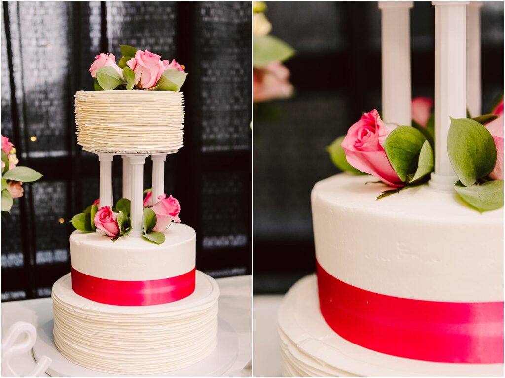 Snohomish Wedding Photographer GSquared Weddings Two-tier wedding cake with textured white frosting. The top tier is supported by pillars and adorned with pink roses and green leaves. A bright pink ribbon wraps around the base of each tier. Black backdrop with pink floral accents on the side. Serving Seattle, Snohomish and Orlando