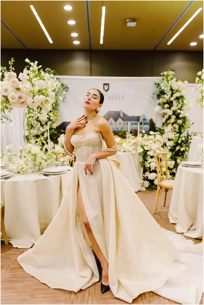 Snohomish Wedding Photographer GSquared Weddings Woman in a glamorous strapless gown poses confidently in an elegant setting adorned with white flowers and greenery. She holds a playful expression with eyes closed, and the atmosphere is sophisticated and luxurious. Serving Seattle, Snohomish and Orlando