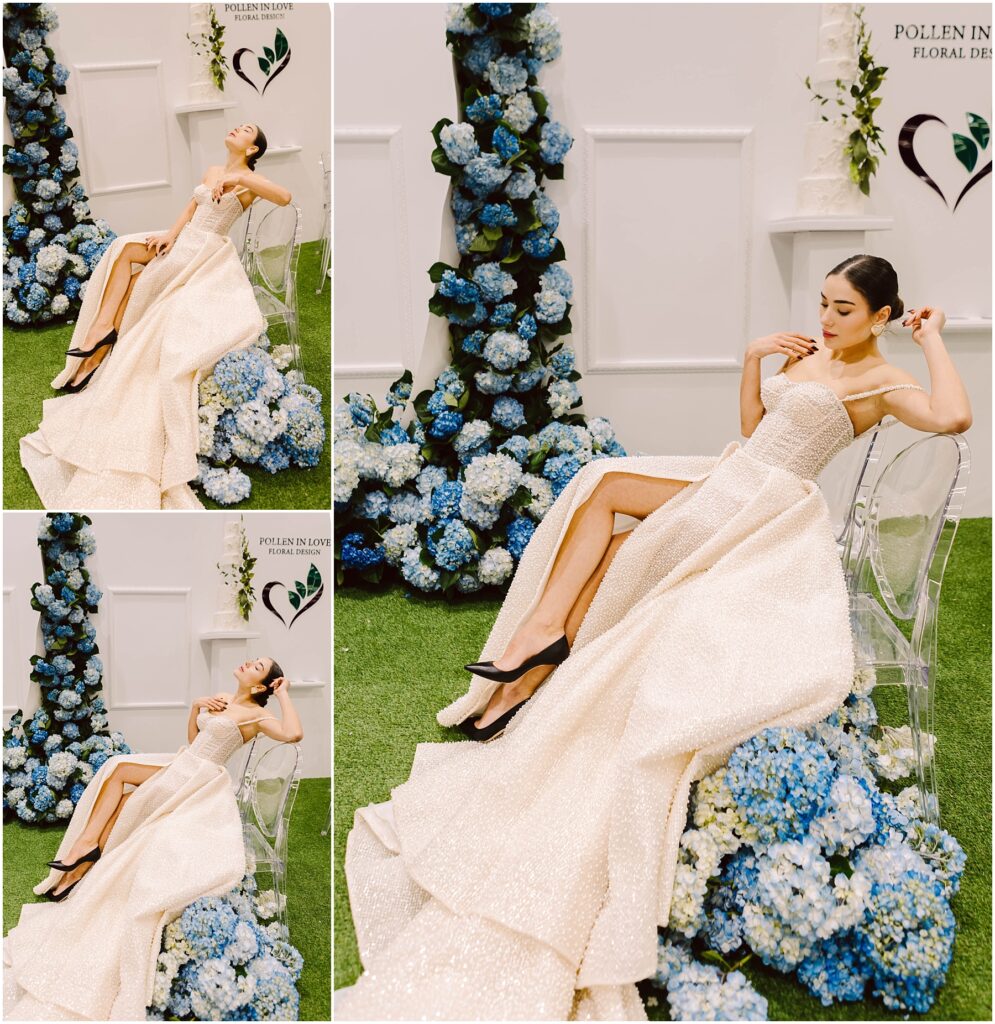 Snohomish Wedding Photographer GSquared Weddings A woman in a shimmering white gown with a high slit poses on a clear chair. The background features blue hydrangeas and white flowers against a white wall with two hearts. Grass covers the floor, creating a fresh, elegant scene. Serving Seattle, Snohomish and Orlando
