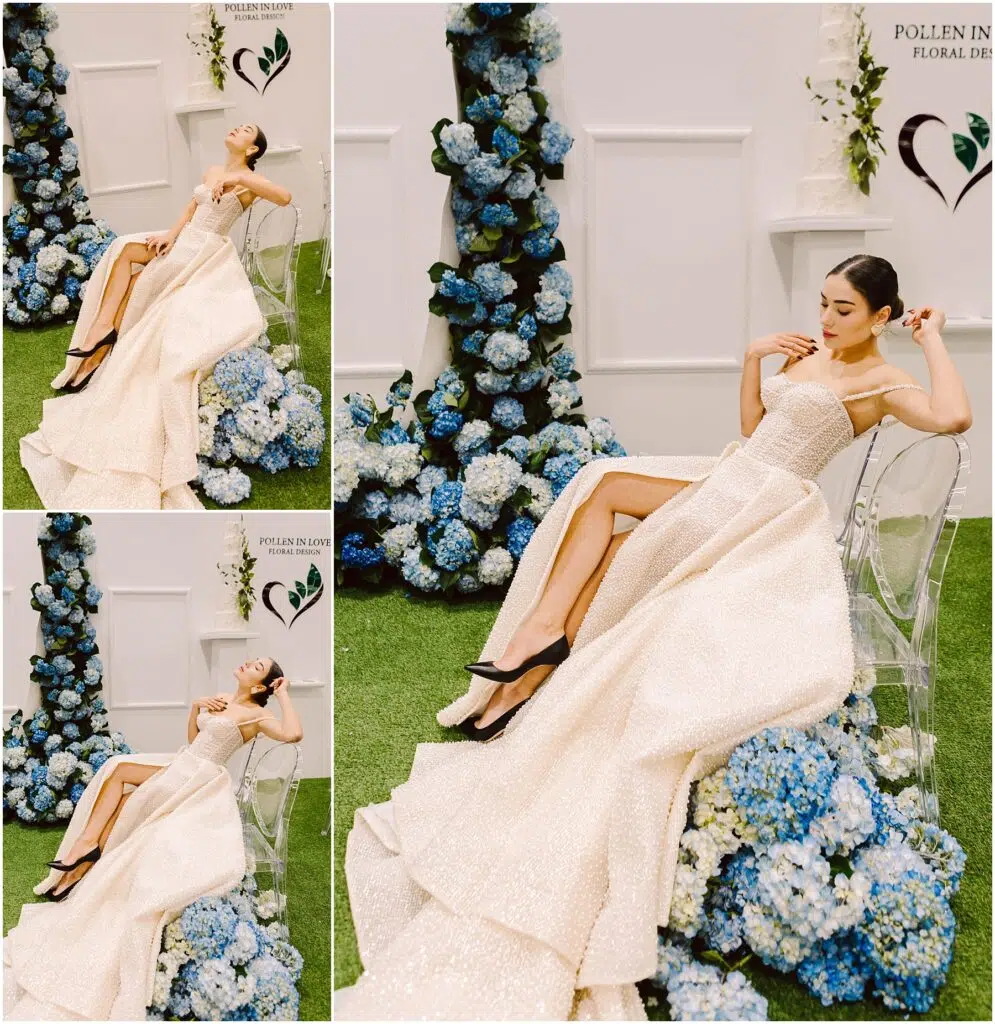 Snohomish Wedding Photographer GSquared Weddings A woman in a shimmering white gown with a high slit poses on a clear chair. The background features blue hydrangeas and white flowers against a white wall with two hearts. Grass covers the floor, creating a fresh, elegant scene. Serving Seattle, Snohomish and Orlando