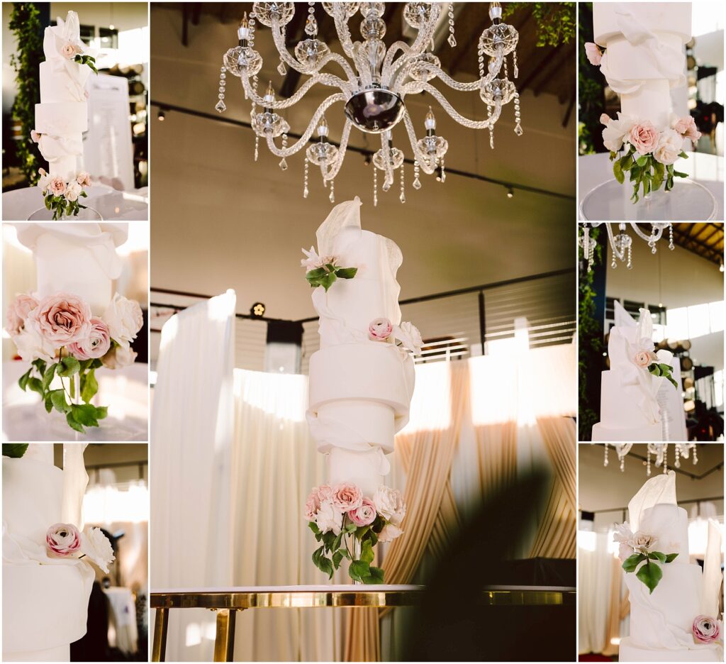 Snohomish Wedding Photographer GSquared Weddings A multi-tiered white wedding cake with elaborate swirling fondant designs, adorned with pink roses. The cake is displayed on a reflective table beneath a sparkling crystal chandelier, surrounded by draped curtains. Serving Seattle, Snohomish and Orlando