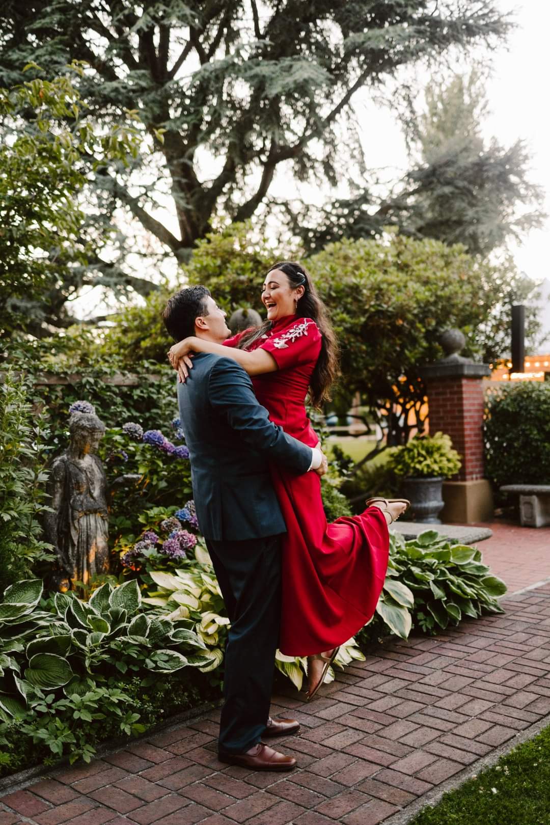 Snohomish Wedding Photographer GSquared Weddings A man in a suit joyfully lifts a woman in a red dress as they pose amidst the gardens lush greenery and vibrant flowers The woman is laughing radiating happiness with a stone statue nearby on the brick path Serving Seattle Snohomish and Orlando Snohomish Wedding Photographer GSquared Weddings A man in a suit joyfully lifts a woman in a red dress as they pose amidst the gardens lush greenery and vibrant flowers The woman is laughing radiating happiness with a stone statue nearby on the brick path Serving Seattle Snohomish and Orlando