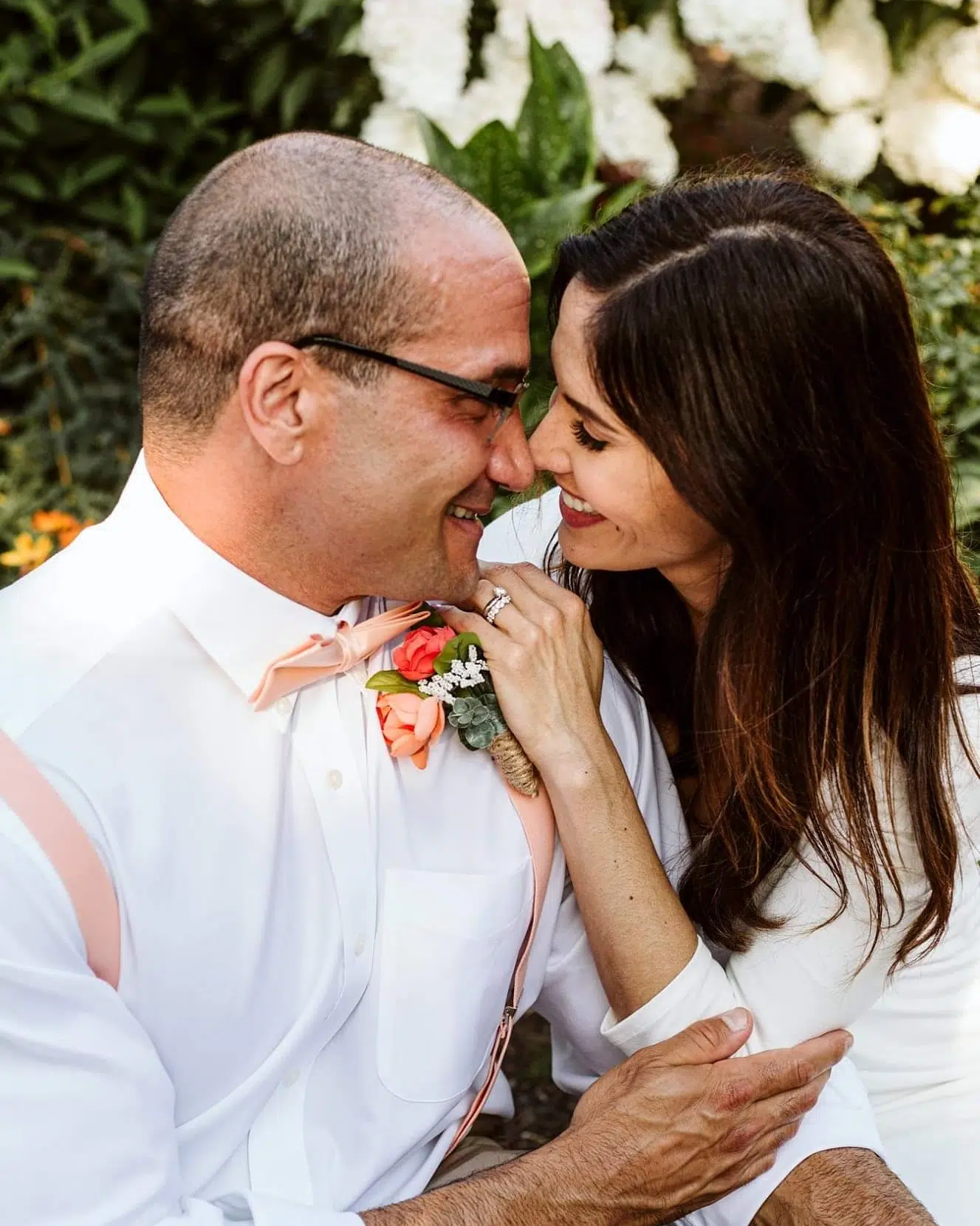 Snohomish Wedding Photographer GSquared Weddings A couple smiling and posing in white attire leans close outdoors The man sports glasses a peach bow tie and suspenders while the woman gently rests her hand on his shoulder showcasing a ring Bright flowers and greenery backdrop them Serving Seattle Snohomish and Orlando Snohomish Wedding Photographer GSquared Weddings A couple smiling and posing in white attire leans close outdoors The man sports glasses a peach bow tie and suspenders while the woman gently rests her hand on his shoulder showcasing a ring Bright flowers and greenery backdrop them Serving Seattle Snohomish and Orlando