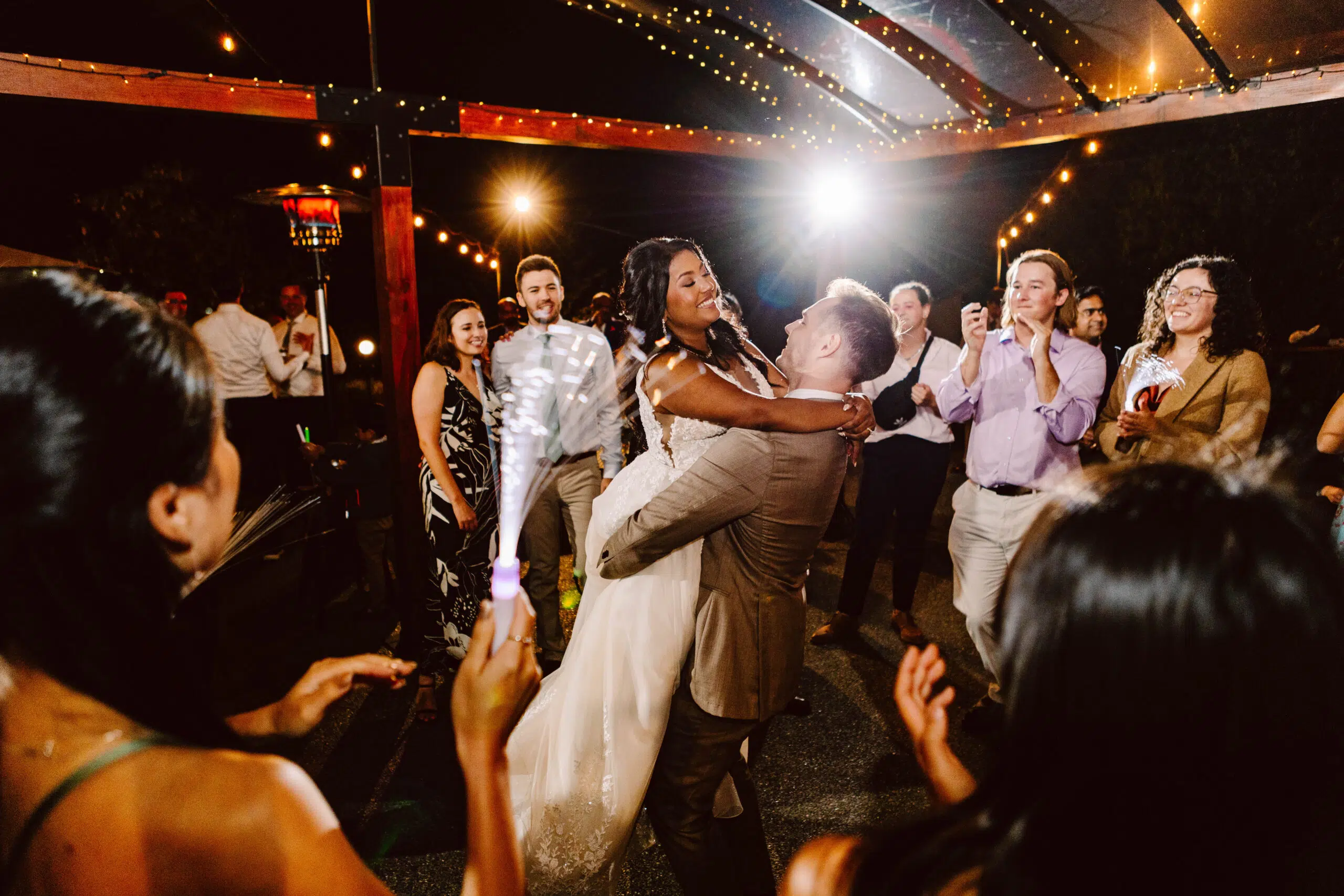 Snohomish Wedding Photographer GSquared Weddings A groom joyfully lifts the bride on a budgetfriendly dance floor surrounded by smiling guests at an outdoor evening celebration String lights illuminate the scene creating a festive atmosphere as they all cheer and capture the moment with their phones Serving Seattle Snohomish and Orlando Snohomish Wedding Photographer GSquared Weddings A groom joyfully lifts the bride on a budget friendly dance floor surrounded by smiling guests at an outdoor evening celebration String lights illuminate the scene creating a festive atmosphere as they all cheer and capture the moment with their phones Serving Seattle Snohomish and Orlando