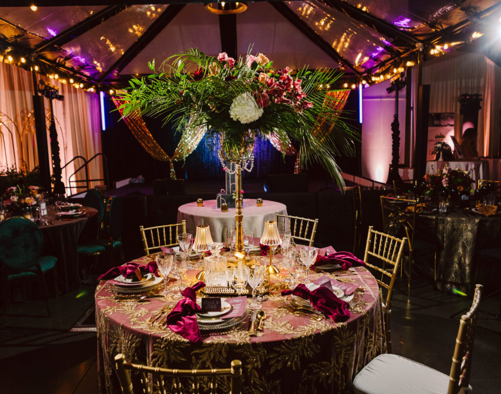 Snohomish Wedding Photographer GSquared Weddings Elegant banquet setup with a round table adorned with floral centerpiece, vibrant pink napkins, and gold chairs. Ambient lighting and clear tent canopy create a warm, luxurious atmosphere. Serving Seattle, Snohomish and Orlando