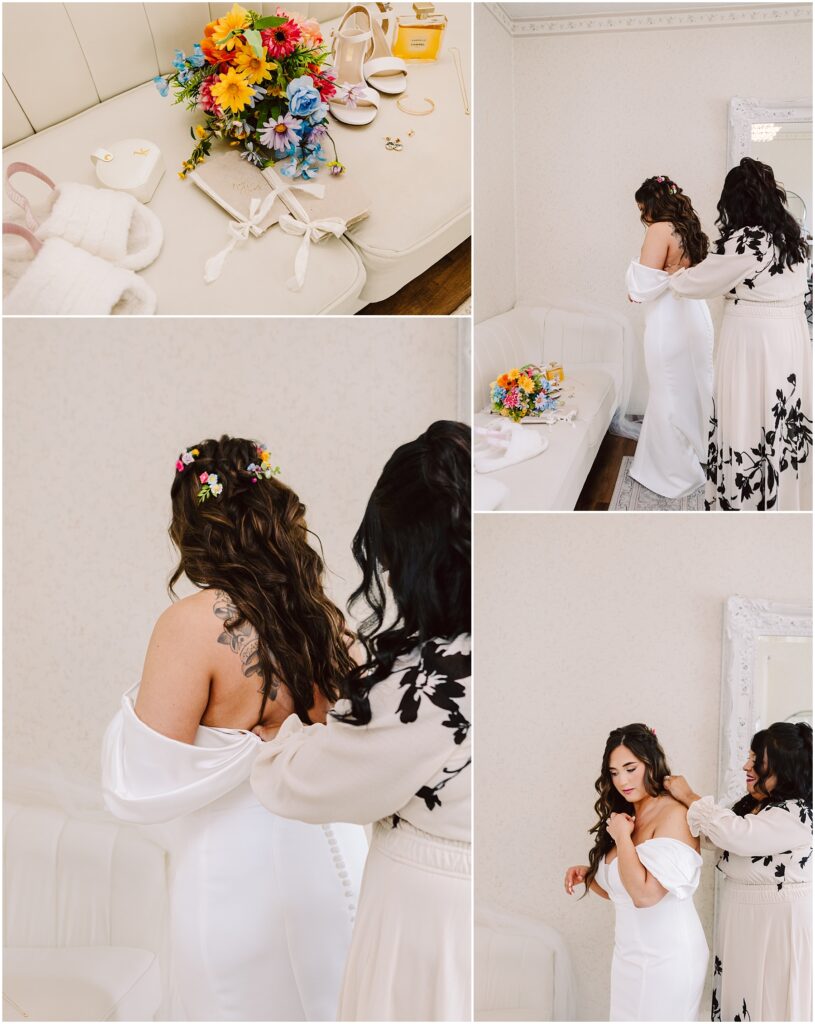 Snohomish Wedding Photographer GSquared Weddings In a room adorned with patterned wallpaper and a white couch, a woman in a white dress is being helped by another in a floral dress. Nearby, bridal accessories and colorful flowers, reminiscent of the vibrant blooms found in Machias, grace the table. Serving Seattle, Snohomish and Orlando