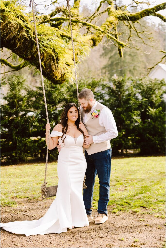 Snohomish Wedding Photographer GSquared Weddings A bride in a white wedding dress stands beside a groom in a shirt and vest with a boutonniere. Theyre outdoors, where the bride clings to a rope swing. The backdrop of greenery hints at the serene beauty one might find in Machias. Serving Seattle, Snohomish and Orlando