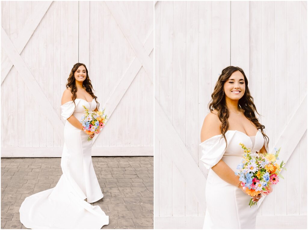 Snohomish Wedding Photographer GSquared Weddings Amidst a rustic white wooden backdrop in Machias, the bride dazzles in an elegant white gown. She clutches a vibrant bouquet of colorful flowers, her long, wavy hair cascading over her shoulders. The dress boasts off-the-shoulder sleeves and a sweeping train as she smiles serenely. Serving Seattle, Snohomish and Orlando