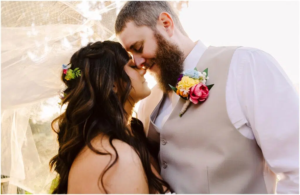 Snohomish Wedding Photographer GSquared Weddings A couple stands embracing, their foreheads touching and eyes closed. The woman, adorned with floral accessories, and the bearded man in a vest with a flower boutonniere, share a serene moment bathed in the soft sunlight of Machias. Serving Seattle, Snohomish and Orlando