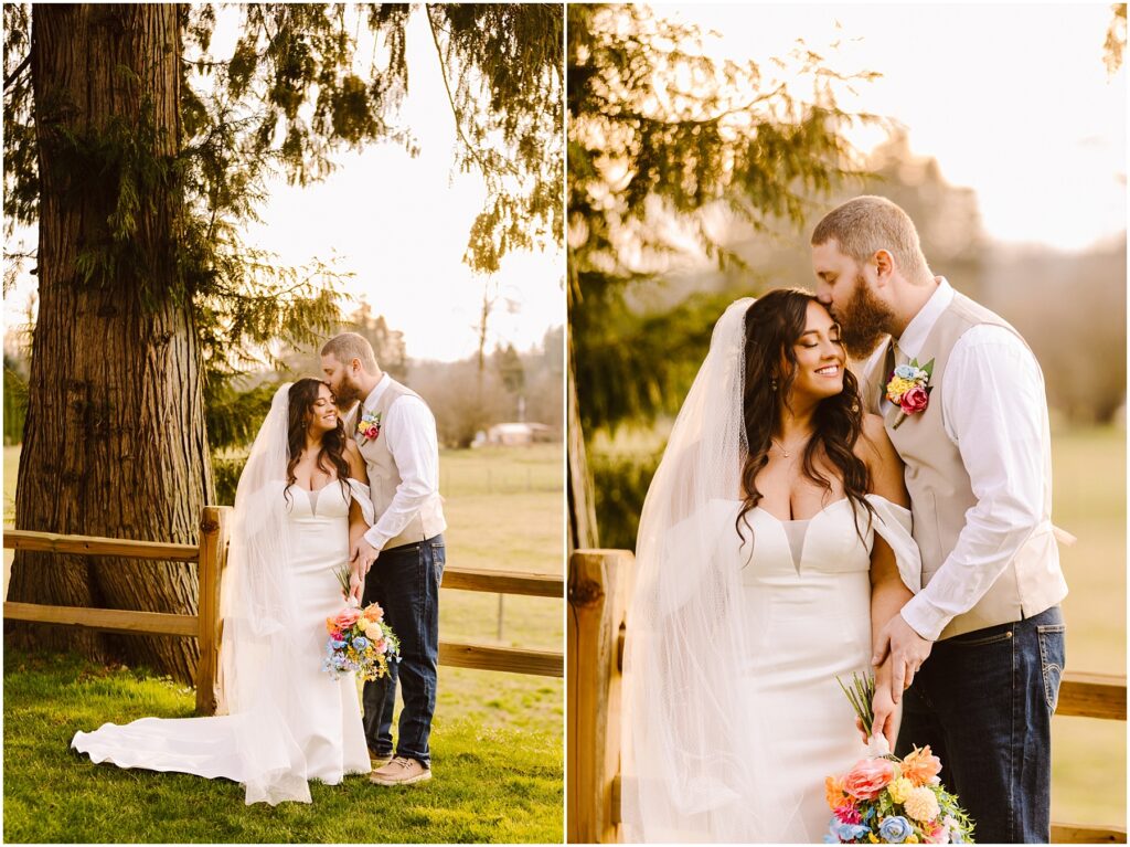 Snohomish Wedding Photographer GSquared Weddings A bride and groom stand outdoors by a wooden fence in Machias, surrounded by greenery. The bride wears a white dress and holds a vibrant bouquet. The groom, in a vest and jeans, gently kisses her forehead. They both look content and happy. Serving Seattle, Snohomish and Orlando