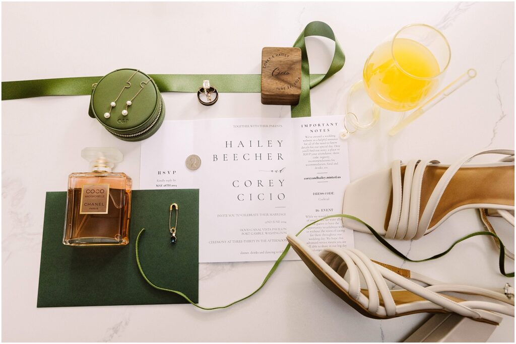 Snohomish Wedding Photographer GSquared Weddings Invitation set for Hailey Beecher and Corey Cicio features delicate perfume, green ribbon, pearl earrings, and a wooden item. An orange drink with a stirring stick complements this Port Gamble affair. Perfect touches for a Summer Wedding; RSVP and important notes included. Serving Seattle, Snohomish and Orlando